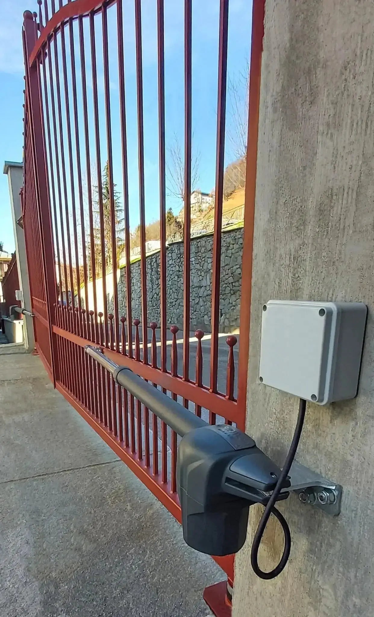 Red swing gate with automated arm motor installed on concrete wall, ideal for secure property access in Qatar.