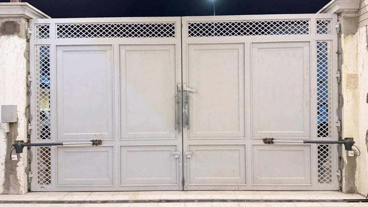 Proteco ASTER 4 NEW swing gate operators with black metal arms mounted on a white paneled double gate with lattice trim