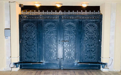 Proteco Telescopic Swing Gate Operator with white housings and dark arms fitted to an ornate black metal double gate