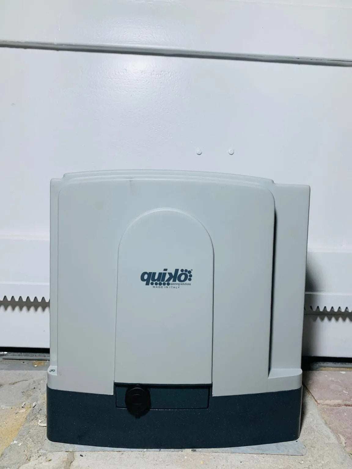 Quiko MOOVY Sliding Gate Operator in a light gray and dark gray plastic housing, with a central Quiko logo and key release.