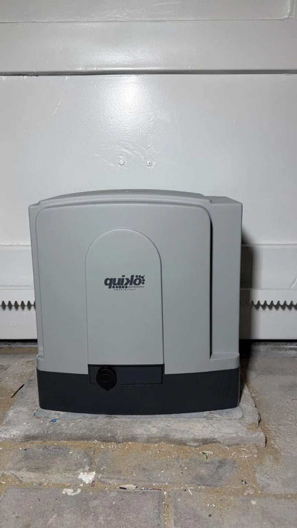 Quiko MOOVY Sliding Gate Operator, gray plastic motor housing with dark base mounted beside a metal gate rack