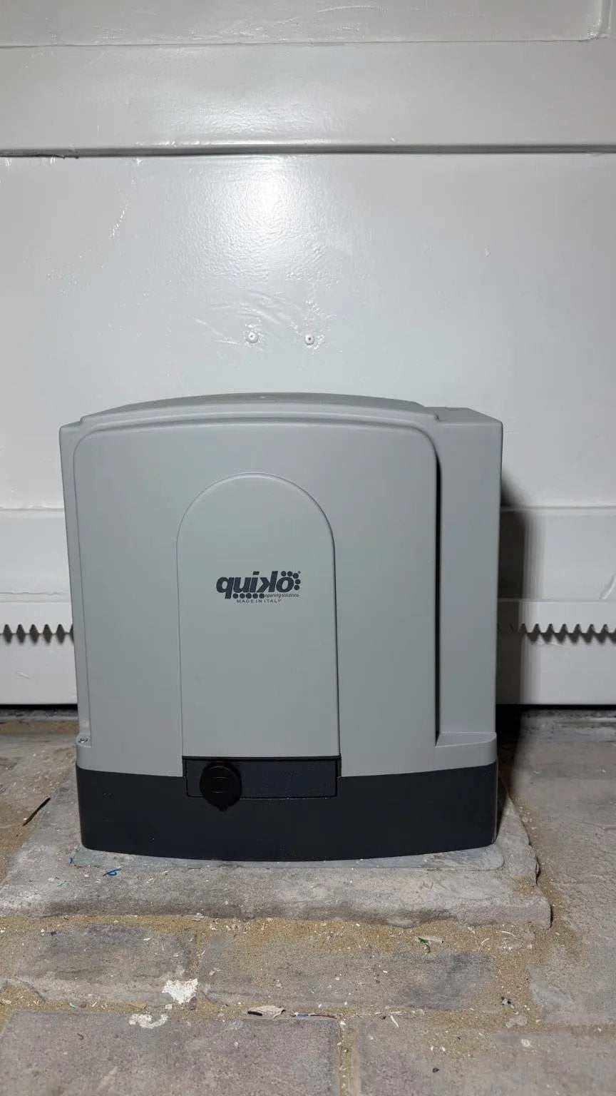 Sliding gate operator, Quiko MOOVY sliding gate operator in Qatar, with a gray molded housing and black base.