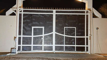 Quiko MOOVY Sliding Gate Operator, white metal motor mounted beside a dark mesh sliding gate with rectangular gridwork