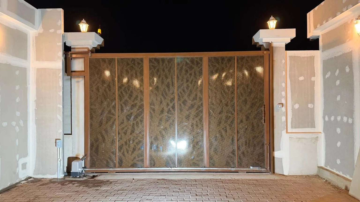 Quiko MOOVY Sliding Gate Operator beside a brown metal sliding gate with patterned mesh panels and a ground-level motor unit.