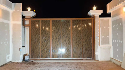 Quiko MOOVY Sliding Gate Operator beside a brown metal sliding gate with patterned mesh panels and a ground-level motor unit.